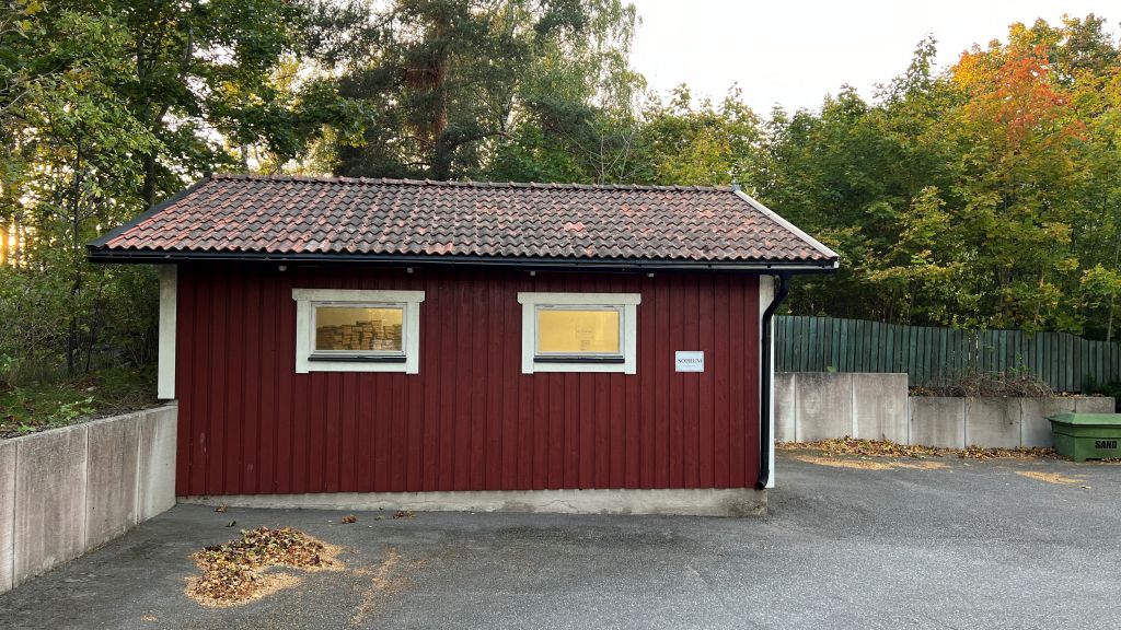En fotografisk bild som fångar utsikten av sophuset beläget på baksidan av fastigheten med adressen Fornminnesvägen 35. Sophuset är en praktisk byggnad för avfallshantering och återvinning och har en tydlig skylt. Inne i byggnaden finns utrymme för avfallsbehållare och kärl, och det är en plats där boende kan deponera sitt hushållsavfall. Bilden visar den omgivande miljön och eventuell tillgänglighet till sophuset från Fornminnesvägen 35.